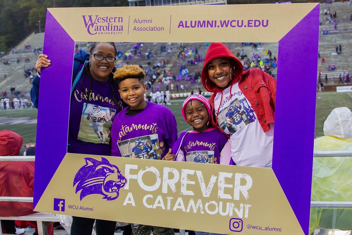Alumni and family holding up a frame for a group photo together in the stadium