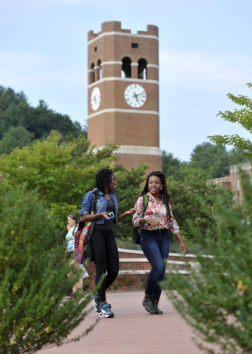 Two students walking around campus with the alumni tower in the background